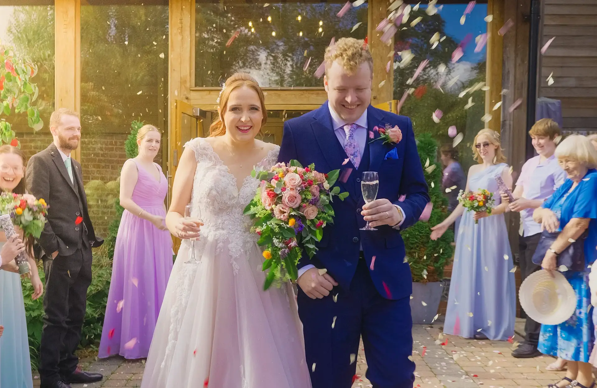 Top Tips for Choosing Your Wedding Videographer - bride & groom confetti thrown over them groom holding a glass and bride holding flowers