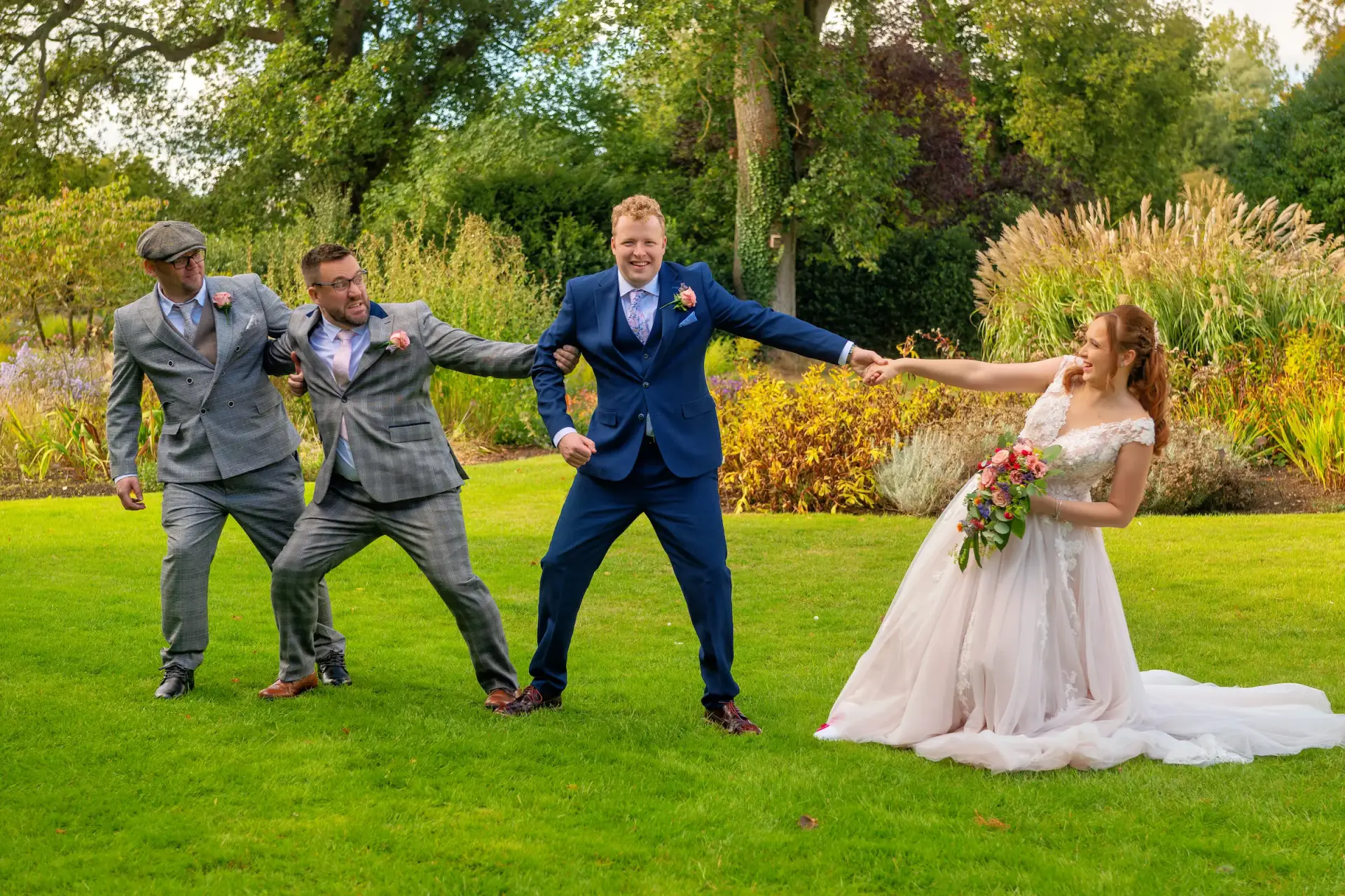 Why hire a videographer for your wedding day Bride pulling the groom from the groomsmen on a sunny lawn